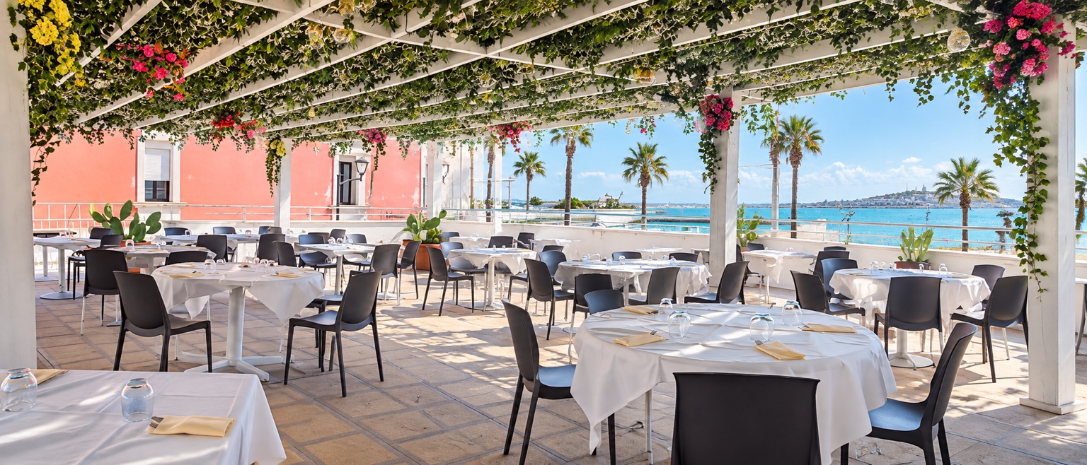 Terrazza panoramica sul mare con pergolato fiorito, tavoli apparecchiati e palme a Porto Cesareo